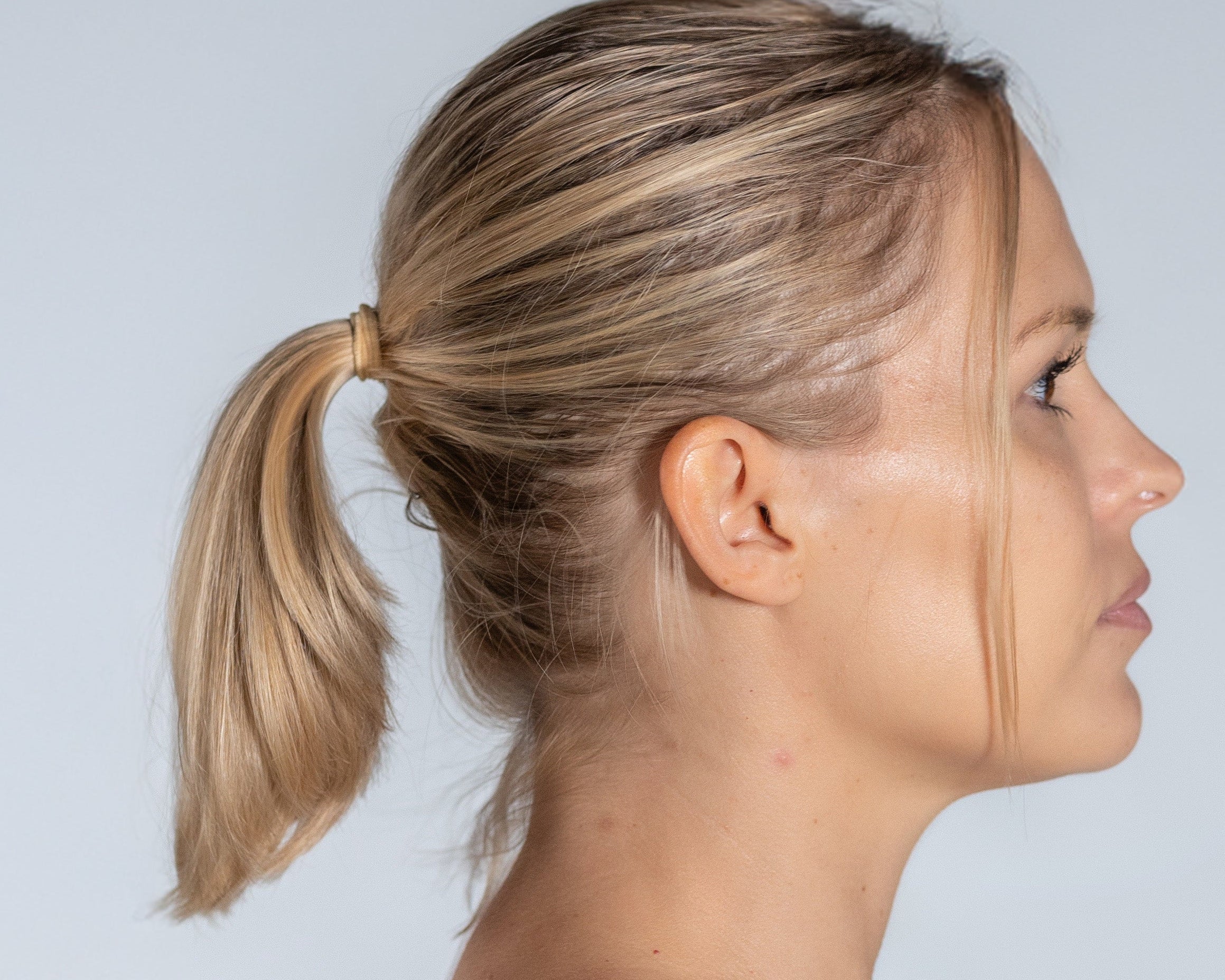Woman with a ponytail wearing a beige tank top against a light gray background