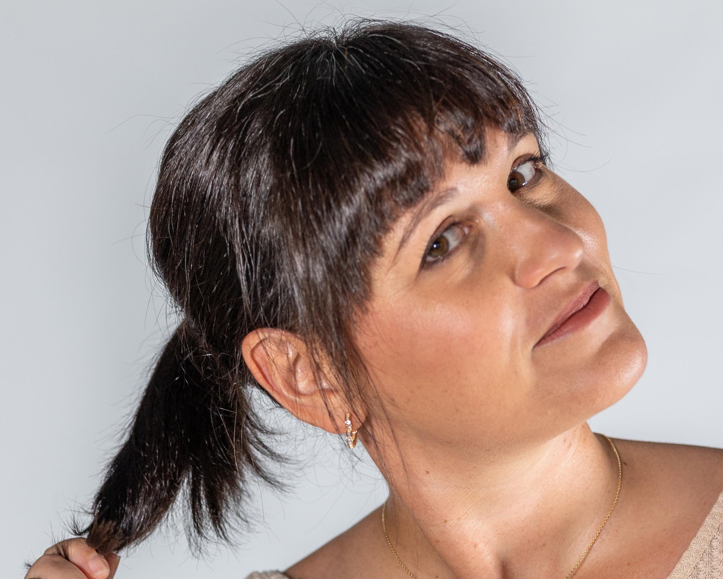 Woman wearing a beige top and blue jeans with a brown belt against a light gray background